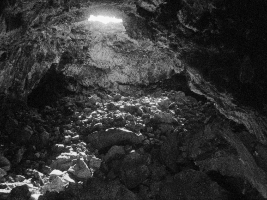 A dark cave interior with scattered rocks and faint light streaming in from a small opening above.